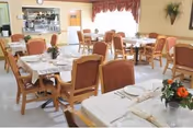 Dining room in a senior facility with round tables, chairs, and floral centerpieces.