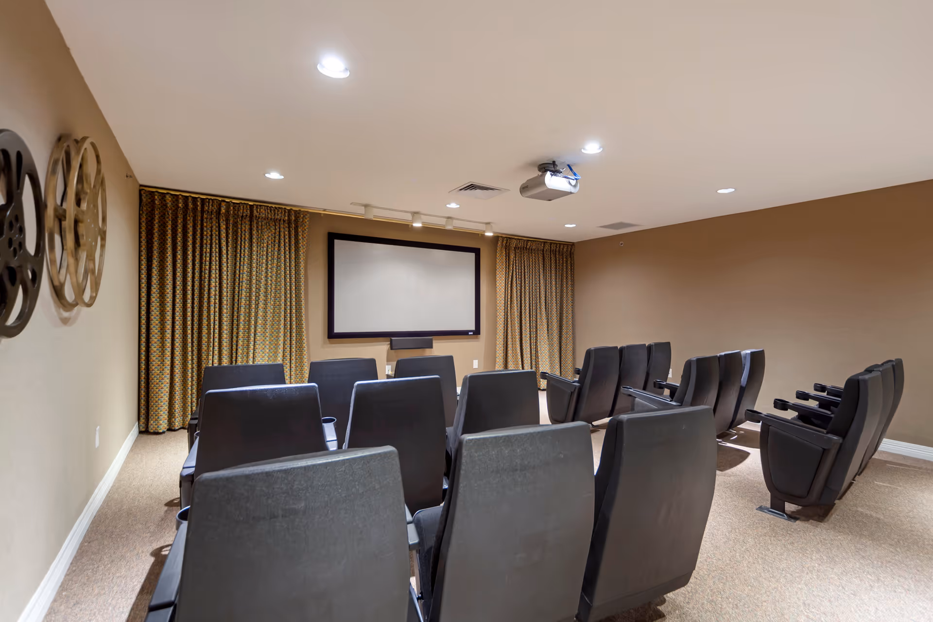 A small screening room with rows of theater-style chairs facing a projector screen and curtains.