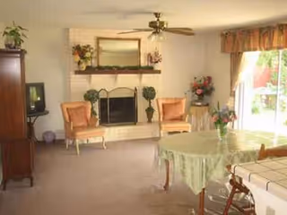 Cozy senior living room with a fireplace, two orange chairs, and a round table.