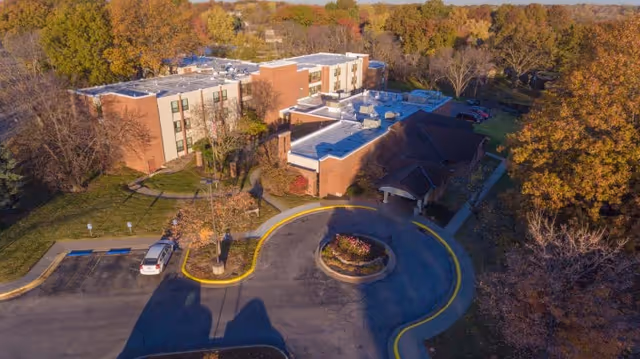 Aerial view of a multi-story brick rehabilitation building with a circular driveway and surrounding autumn trees.