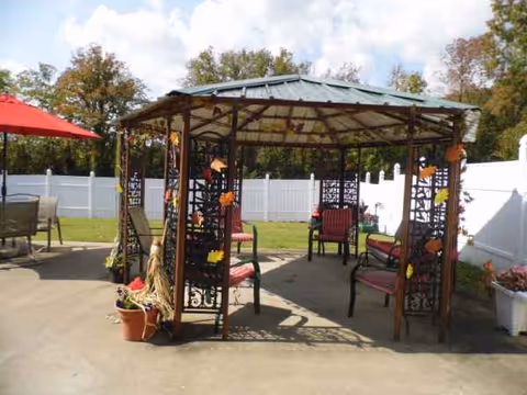 Outdoor gazebo with metal lattice, benches, potted plants, and white privacy fence.