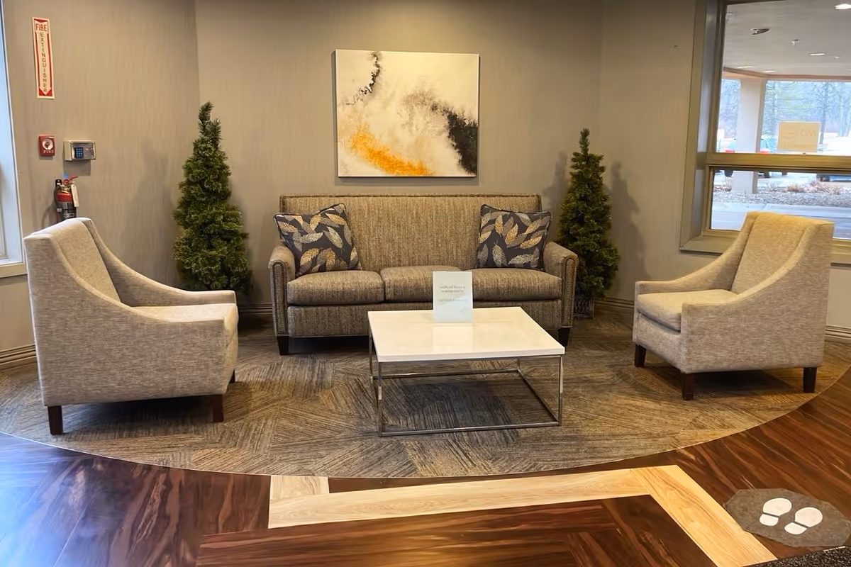 Seating area with a sofa, two armchairs, a coffee table, wall art, and small decorative trees in a lobby-like space.