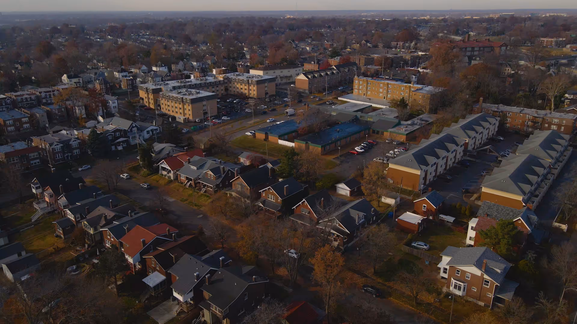 Aerial view of a neighborhood showing houses, rows of apartment buildings, and surrounding streets and parking lots.