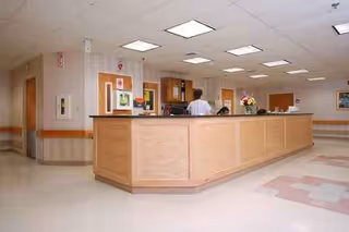 Long wooden reception desk in a care facility lobby with a staff member present.