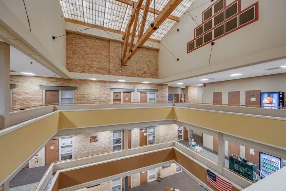 Multi-level interior atrium with open corridors and railings, exposed brick walls, a large skylight ceiling, and a vending machine.