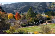 A landscaped hillside view showing several residential buildings and trees with rolling hills in the background.
