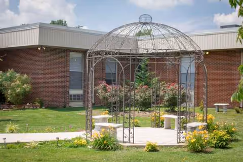 Garden courtyard with a metal gazebo in front of a brick facility building.