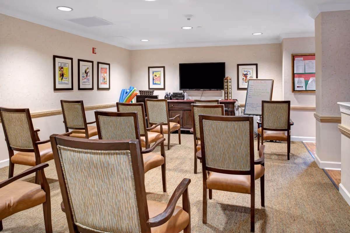 Rows of chairs arranged facing a wall-mounted TV, a cabinet, and a whiteboard in a small activity/meeting room.