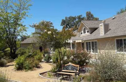 Exterior view of Wild Rose Care Home with garden, walkway, and bench.