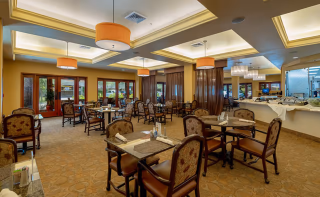 Spacious dining room with multiple set tables and cushioned chairs, warm pendant lighting, and a buffet counter.