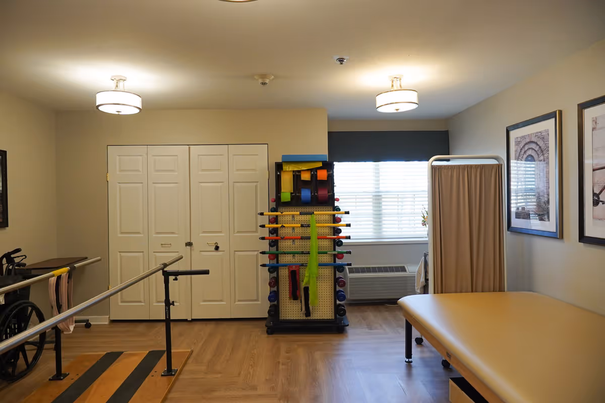 Rehabilitation room with parallel bars, therapy equipment, treatment table, wheelchair and a privacy curtain.