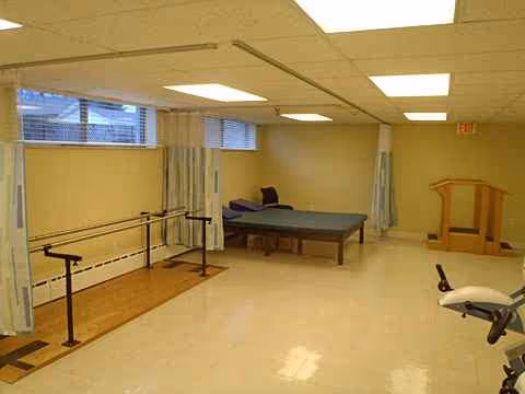 Rehabilitation room inside facility with parallel bars, treatment bed, and exercise equipment.