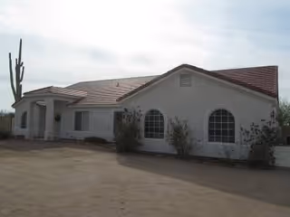 A single-story white senior living facility with arched windows and desert landscaping.