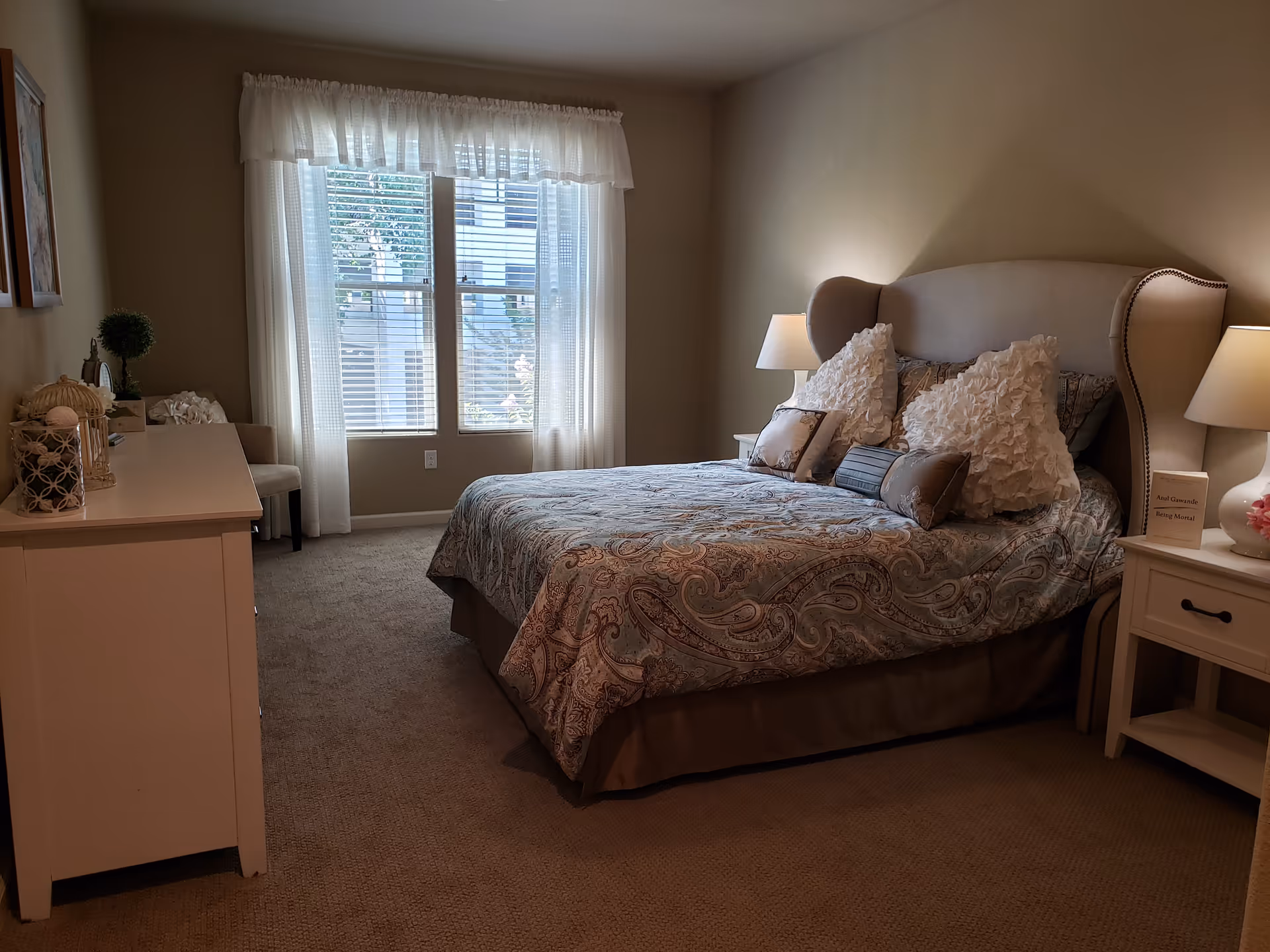 Bedroom with large bed, nightstands, lamps, and window with sheer curtains.