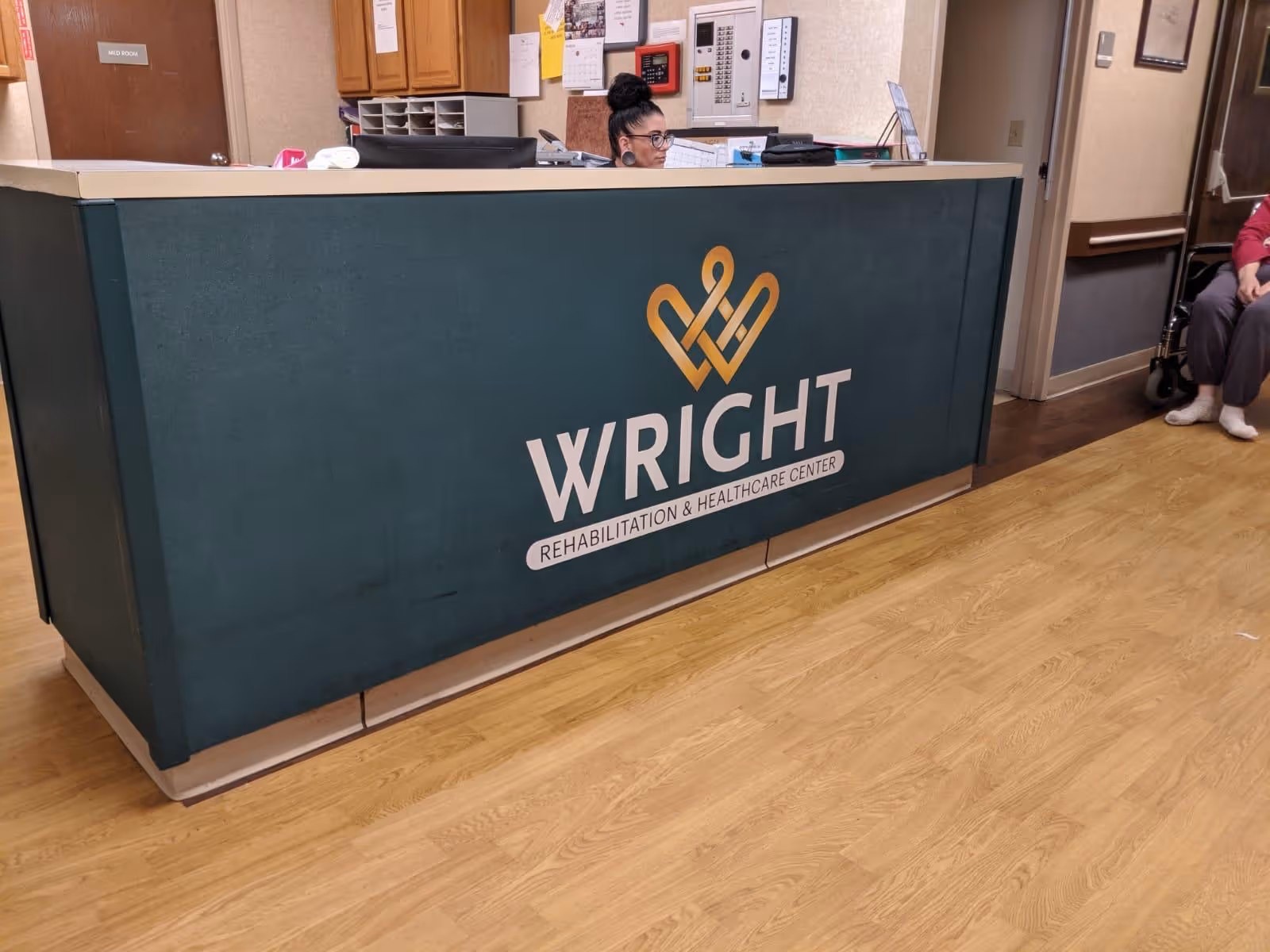 Reception desk with a large 'WRIGHT Rehabilitation & Healthcare Center' logo and a staff member seated behind it in a facility lobby.