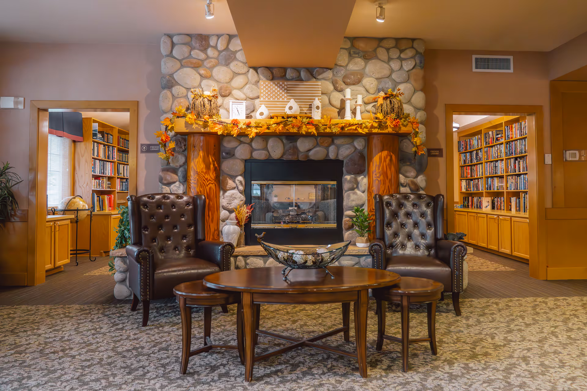 Cozy lounge with two leather armchairs and a coffee table facing a stone fireplace, flanked by bookshelves.