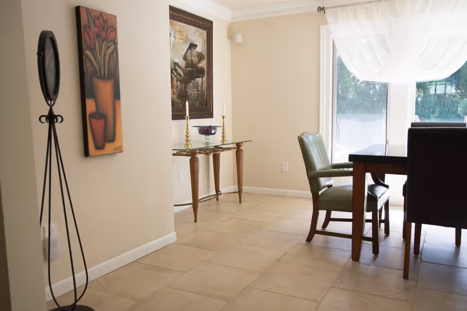 Light-filled dining area with a wooden table, green upholstered chairs, a glass console table and wall art.