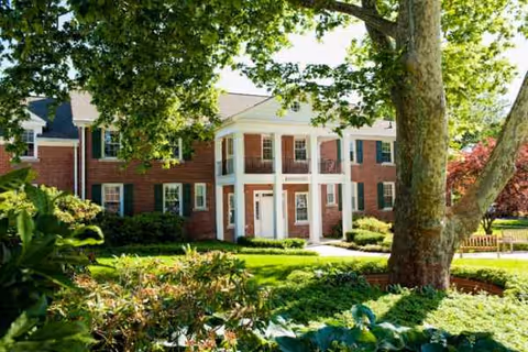A red brick senior living facility with white columns, surrounded by trees and landscaping.