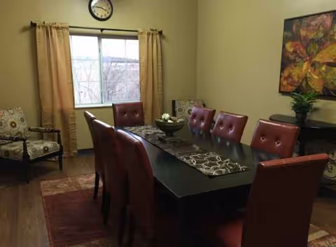 Dining room with a long table, red upholstered chairs, window, and wall art.