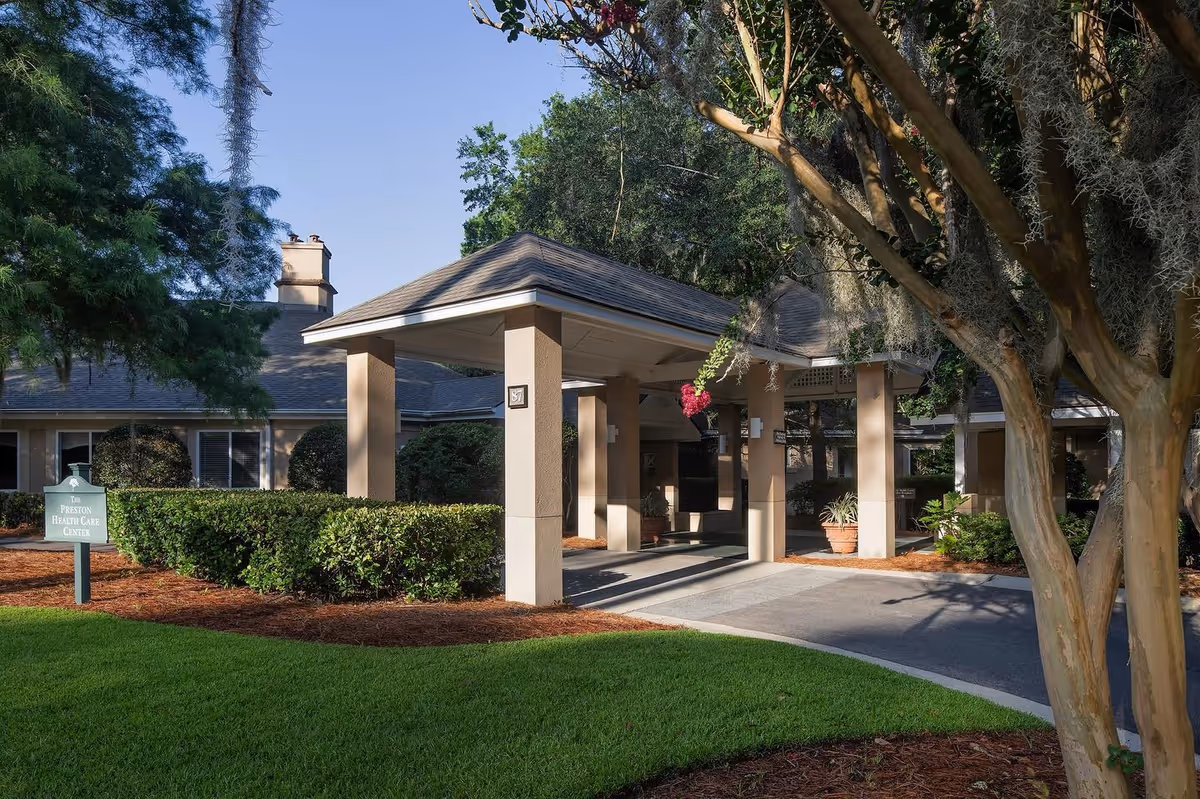 Front entrance of The Preston Health Center showing a covered porte-cochere, landscaped lawn and trees.