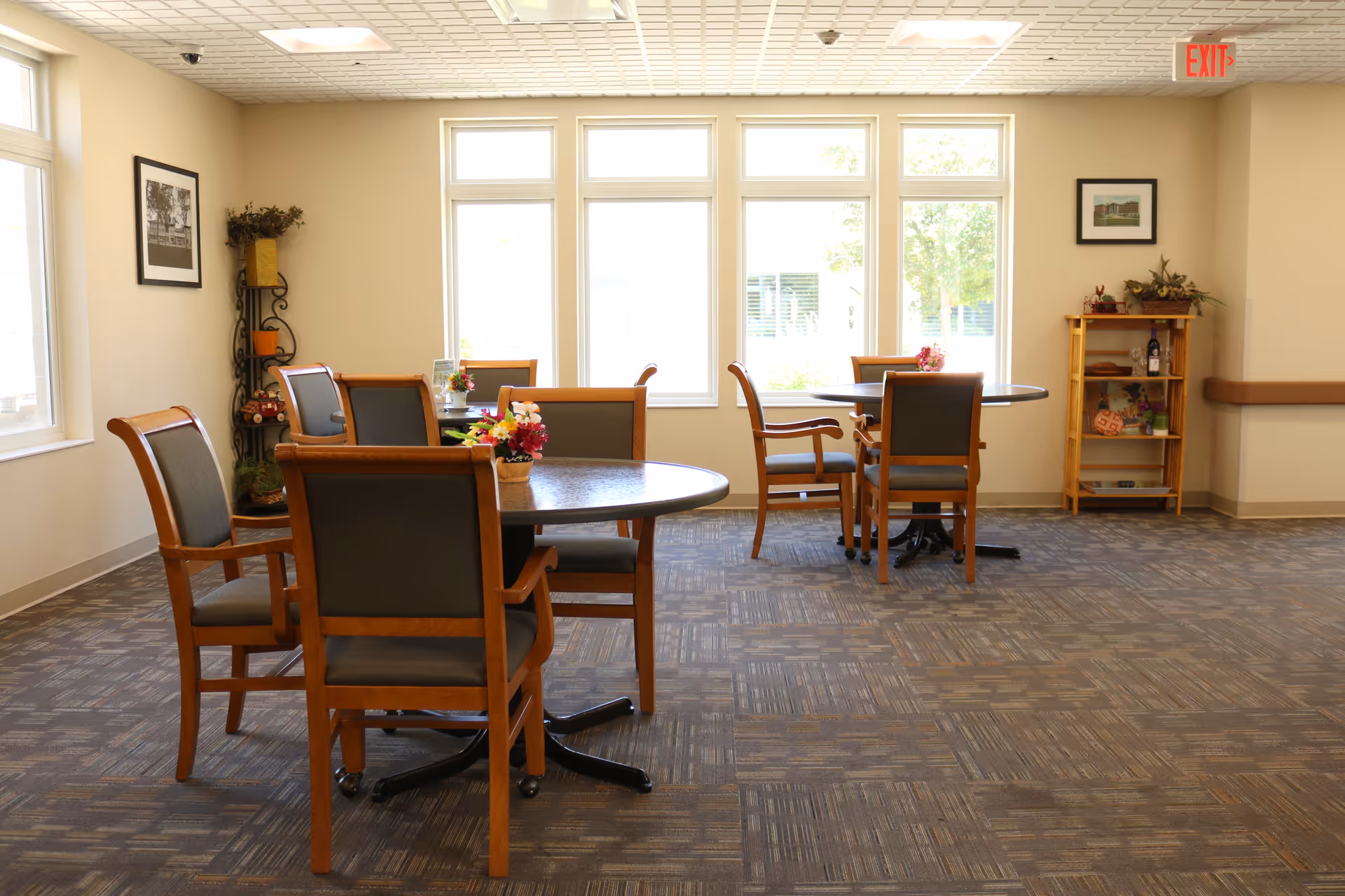 Well-lit common dining area with round tables and chairs arranged near large windows