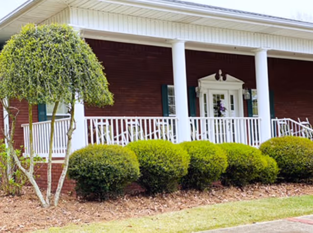 Front view of Mountain Cove senior living facility with brick exterior, white pillars, and manicured shrubs.