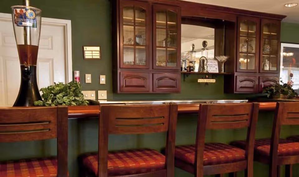 Wooden bar counter with four high-backed stools in front of glass-front cabinets and a mirrored backsplash.