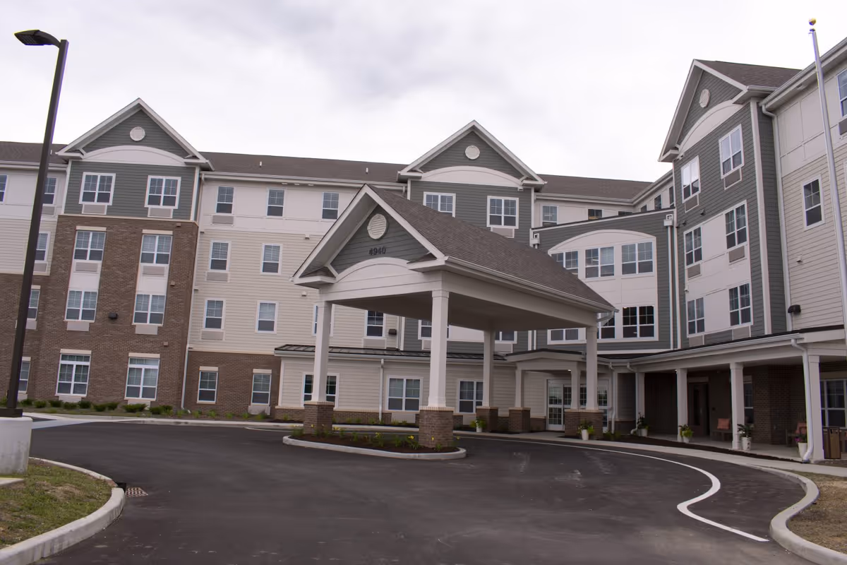 Front exterior of a four-story residential building with a covered drive-up entrance (porte-cochère) and a curved driveway.