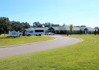 SomerOak Senior Living exterior with curved driveway, buses, and a green lawn.