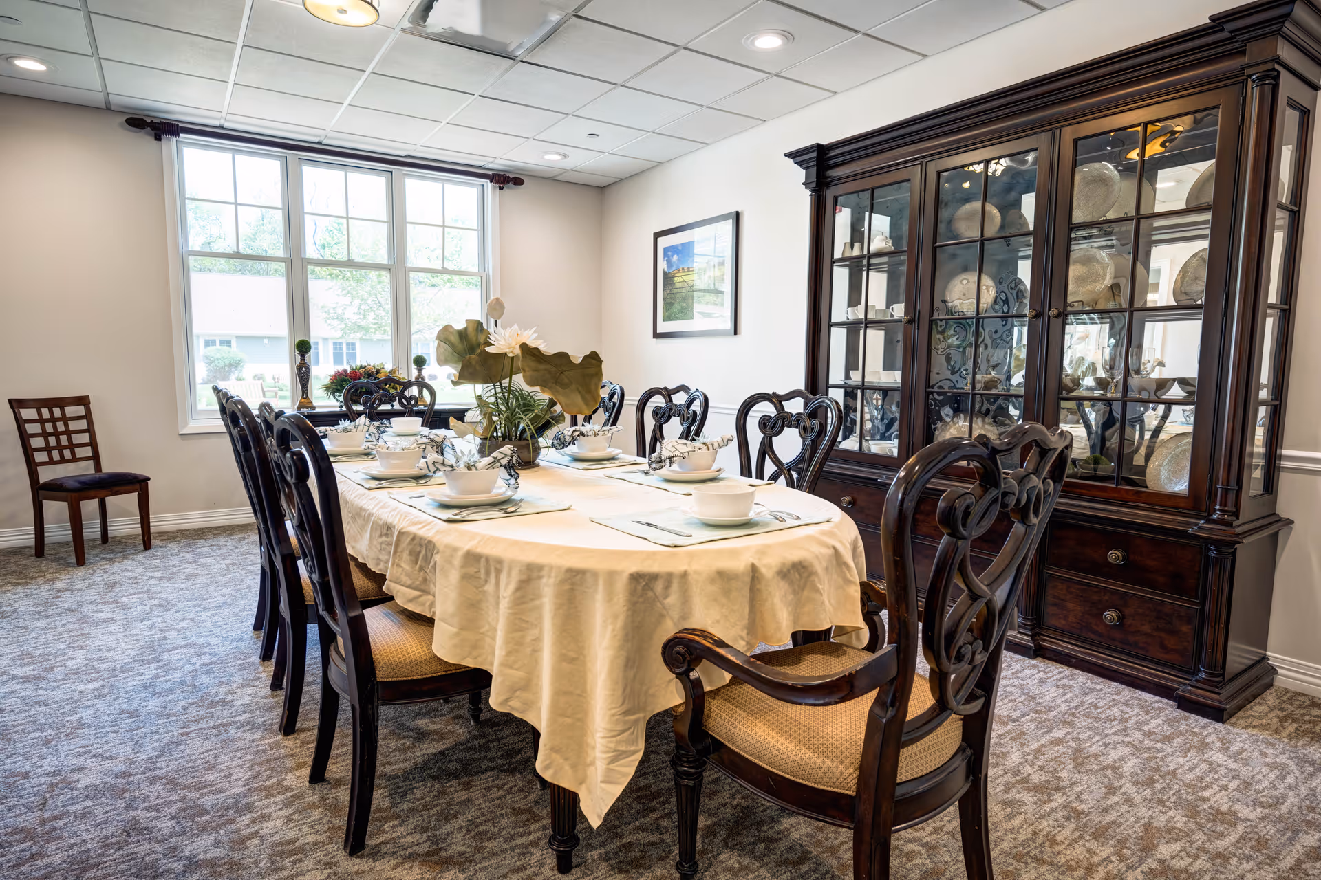 Elegant dining room with a long table set with dishware, ornate wooden chairs, and a large china cabinet by the wall.