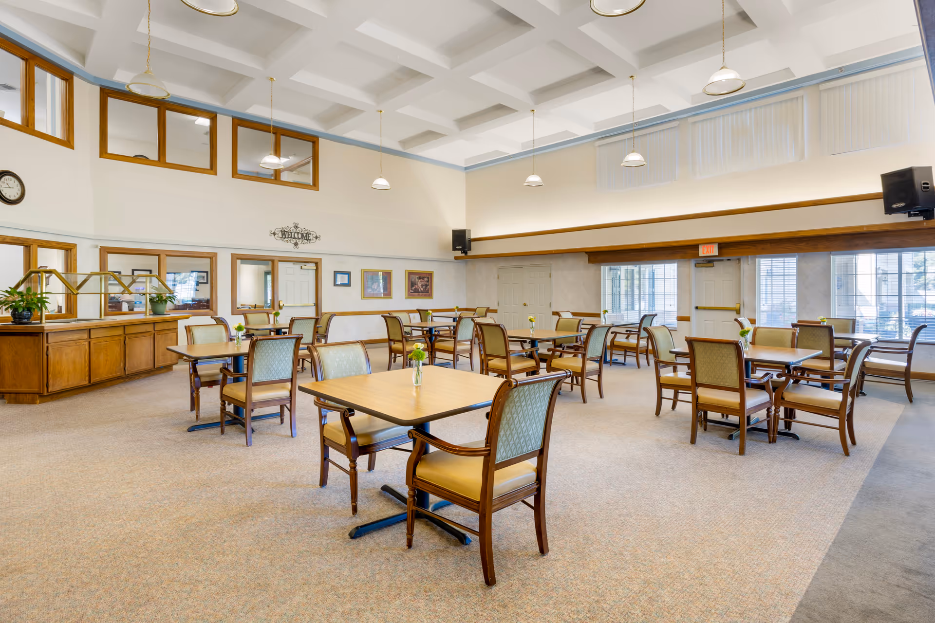 Bright, spacious dining room with multiple wooden tables and chairs, pendant lights, and a serving counter.