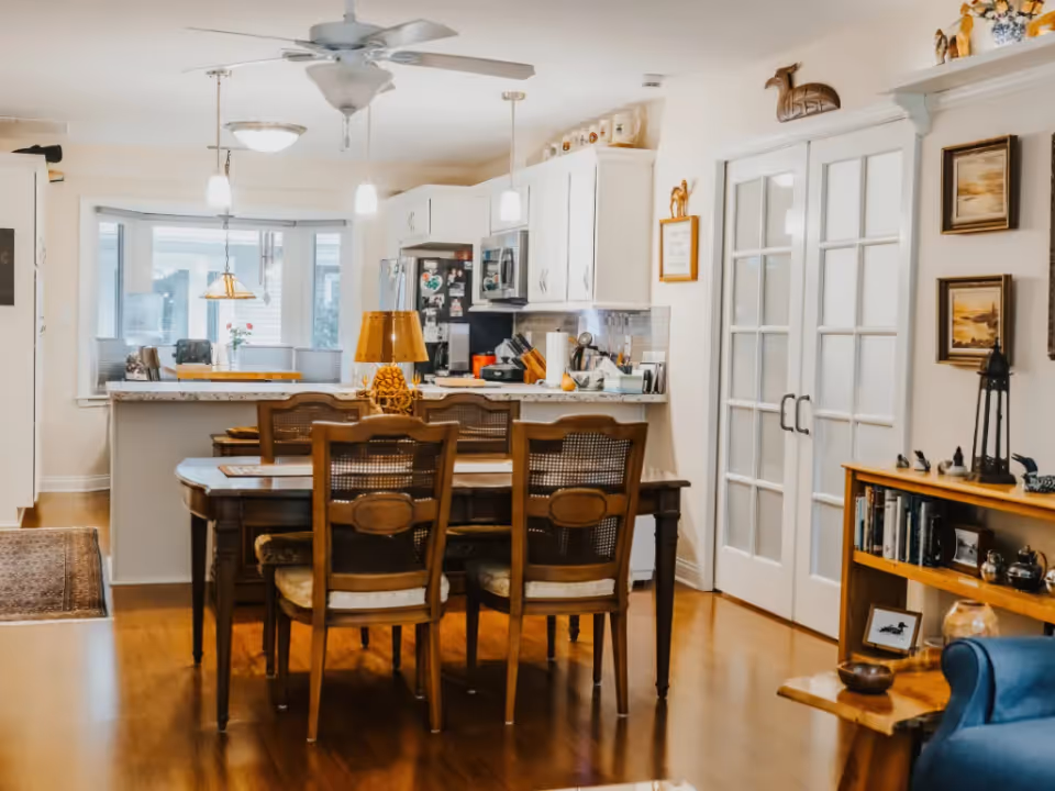 Open-concept dining area with a wooden table and chairs facing a white kitchen and French doors.