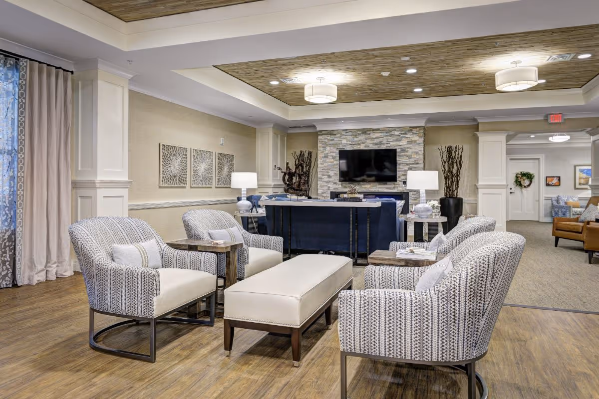 Communal living room with patterned armchairs around a central ottoman, a TV on a stone accent wall, and soft ceiling lighting.