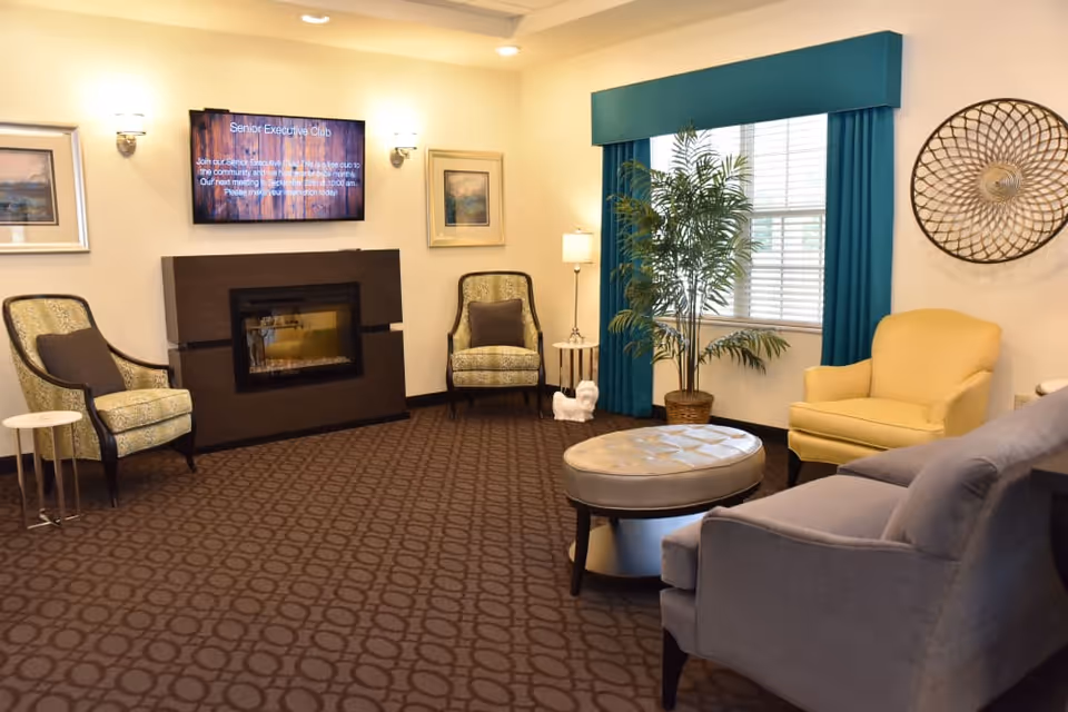 Lounge area with armchairs, a sofa and ottoman, fireplace, wall-mounted TV, and a window with teal curtains.