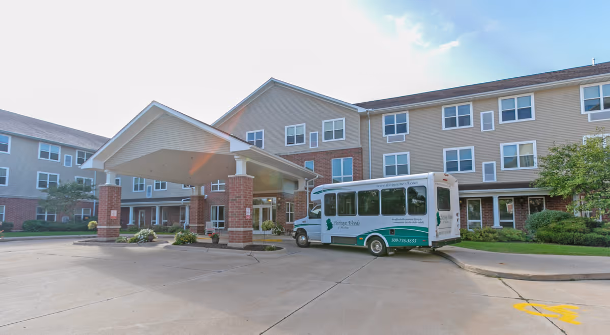 Front entrance of a senior living facility with a covered porte-cochere and a parked shuttle bus.