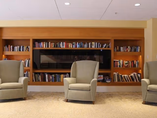 Three upholstered armchairs arranged in front of built-in wooden bookshelves filled with books and a recessed dark panel.