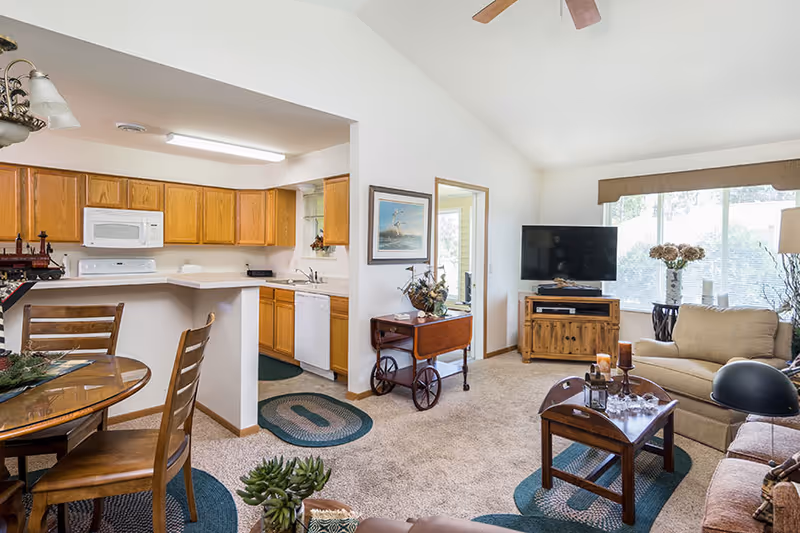 Open-plan living room and kitchen with a dining table, sofa, coffee table, TV, and oak kitchen cabinets.