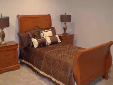 Wooden bed with brown bedding, two nightstands, and lamps in a cozy bedroom.