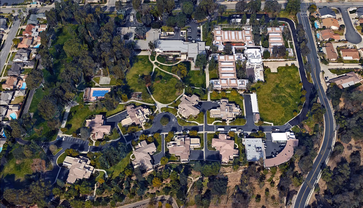 Aerial view of the Masonic Homes facility showing multiple buildings, parking lots, green lawns, trees, pathways, and surrounding residential neighborhood.