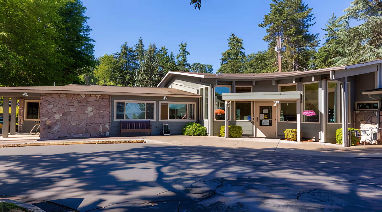 Exterior view of Hillside Heights Rehabilitation Center building with stone and glass facade, surrounded by trees and greenery under a clear blue sky.