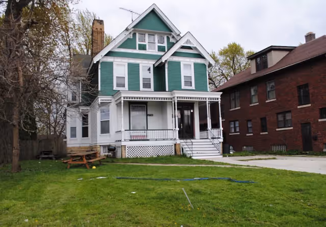 Green and white Victorian-style house with a front porch and a grassy yard.