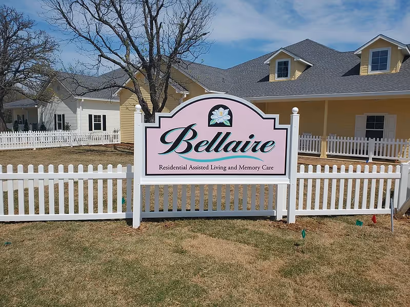 Pink Bellaire sign in front of a beige assisted living building with white fencing.