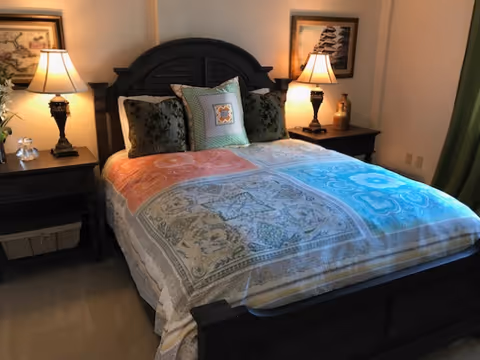 Cozy bedroom with a dark wooden bed dressed in a multicolored patterned comforter, flanked by two nightstands with lamps.