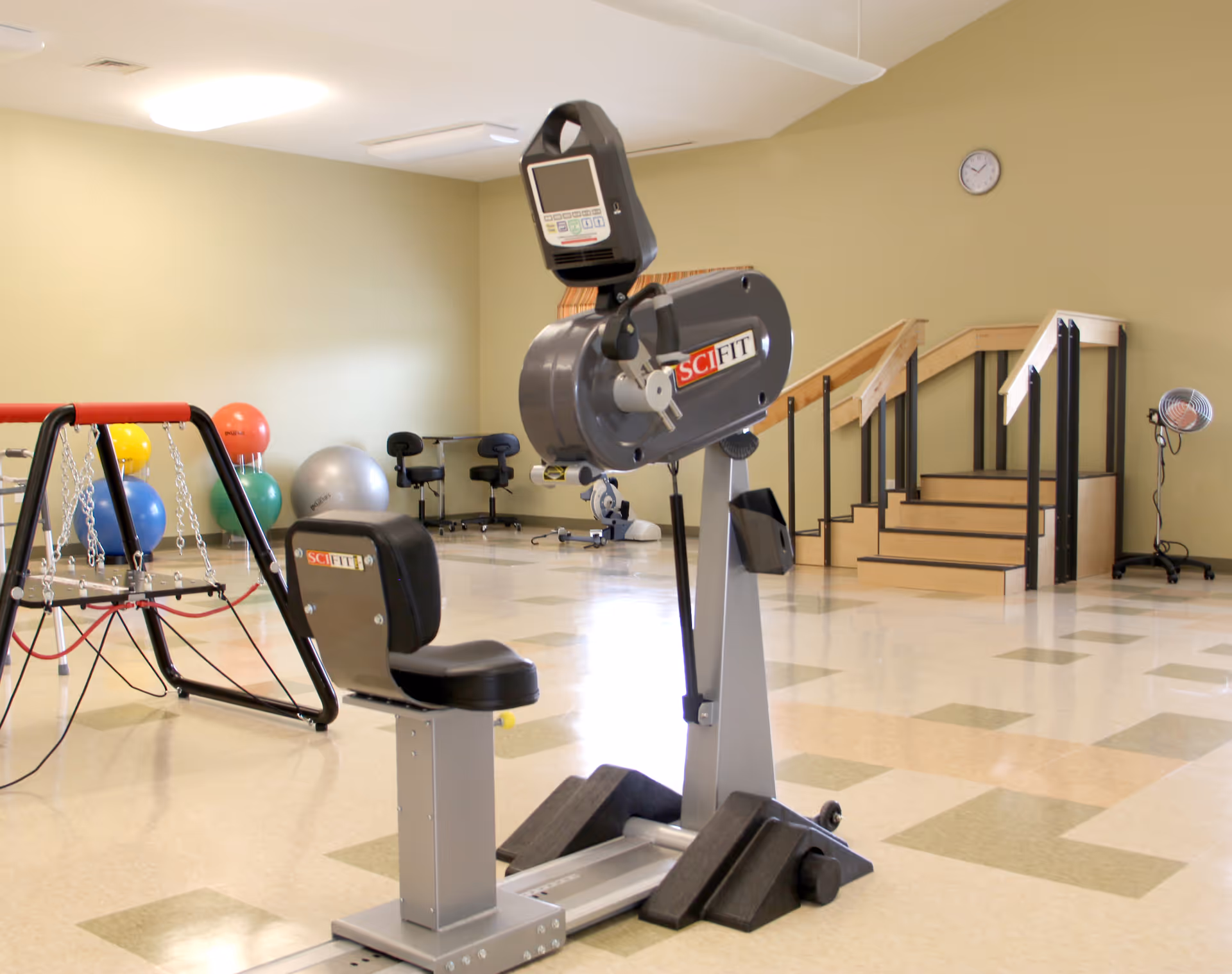 An indoor therapy/exercise room with a SciFit exercise machine, therapy balls, balance equipment, and a practice stair set.