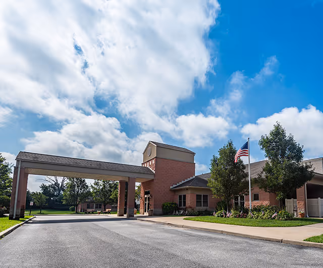 Front entrance of the Spring Oak at Berlin building with a covered porte-cochere, American flag, and landscaped grounds under a blue sky.