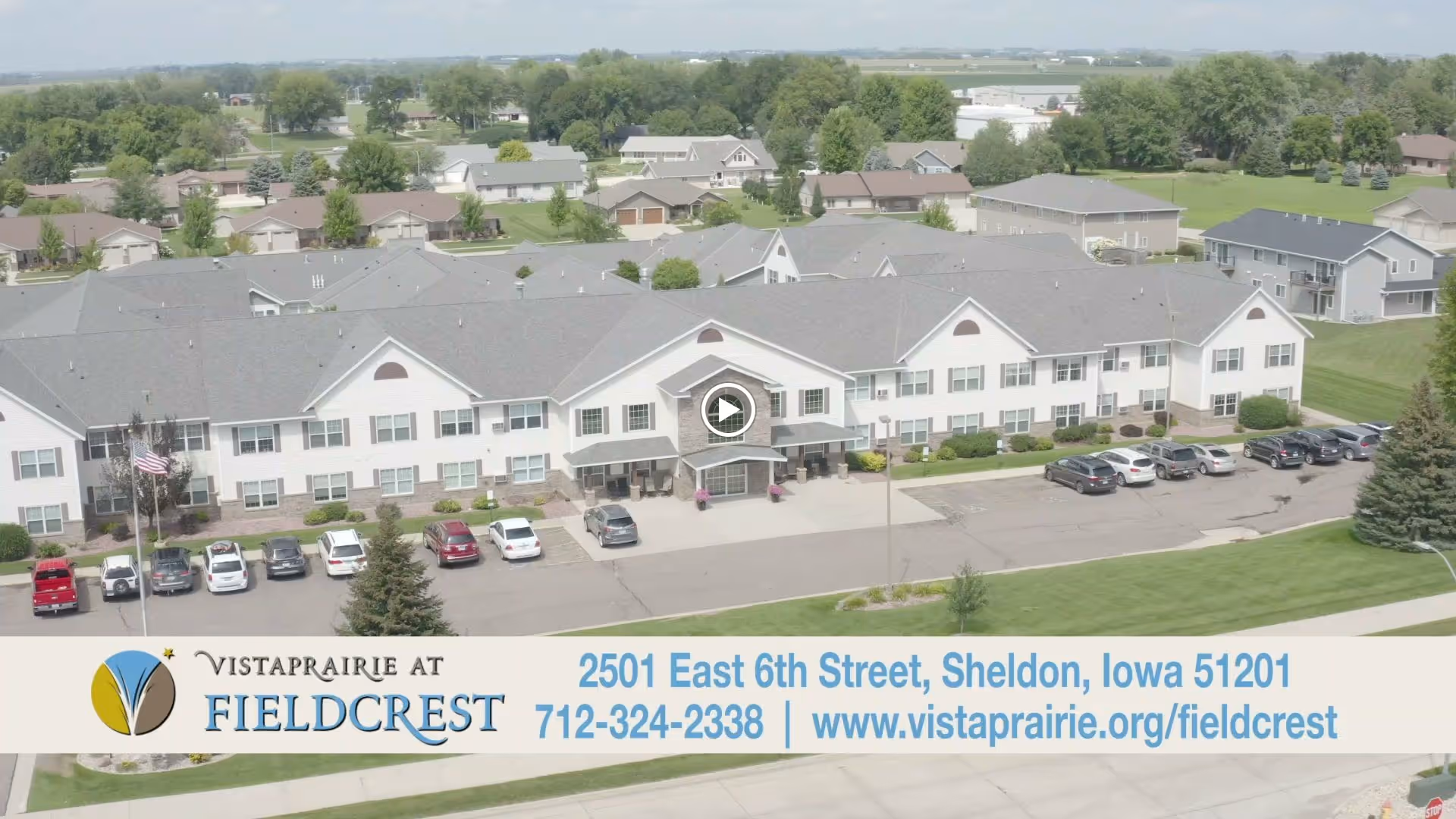 Aerial view of the Vista Prairie at Fieldcrest senior living building with parking lot and surrounding neighborhood, and a contact banner along the bottom.