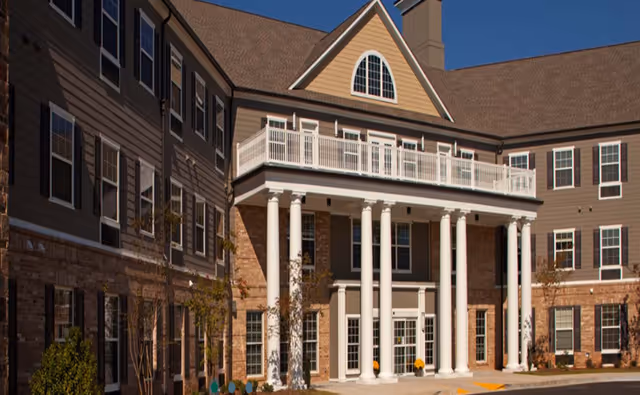 Exterior view of Canterfield Senior Living building featuring a multi-story structure with large white columns supporting a balcony, numerous windows, and a clear blue sky in the background.