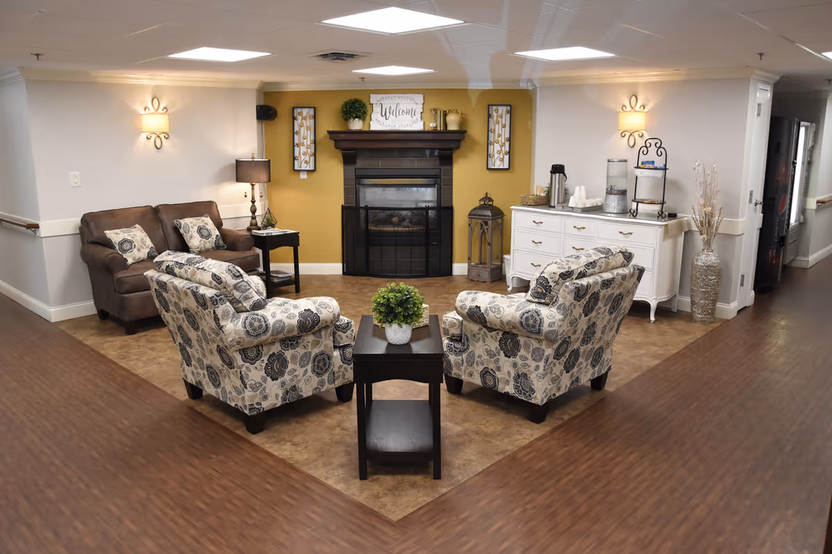 Comfortable common-area seating with two patterned armchairs, a loveseat, coffee table, fireplace and sideboard in a hallway lounge.