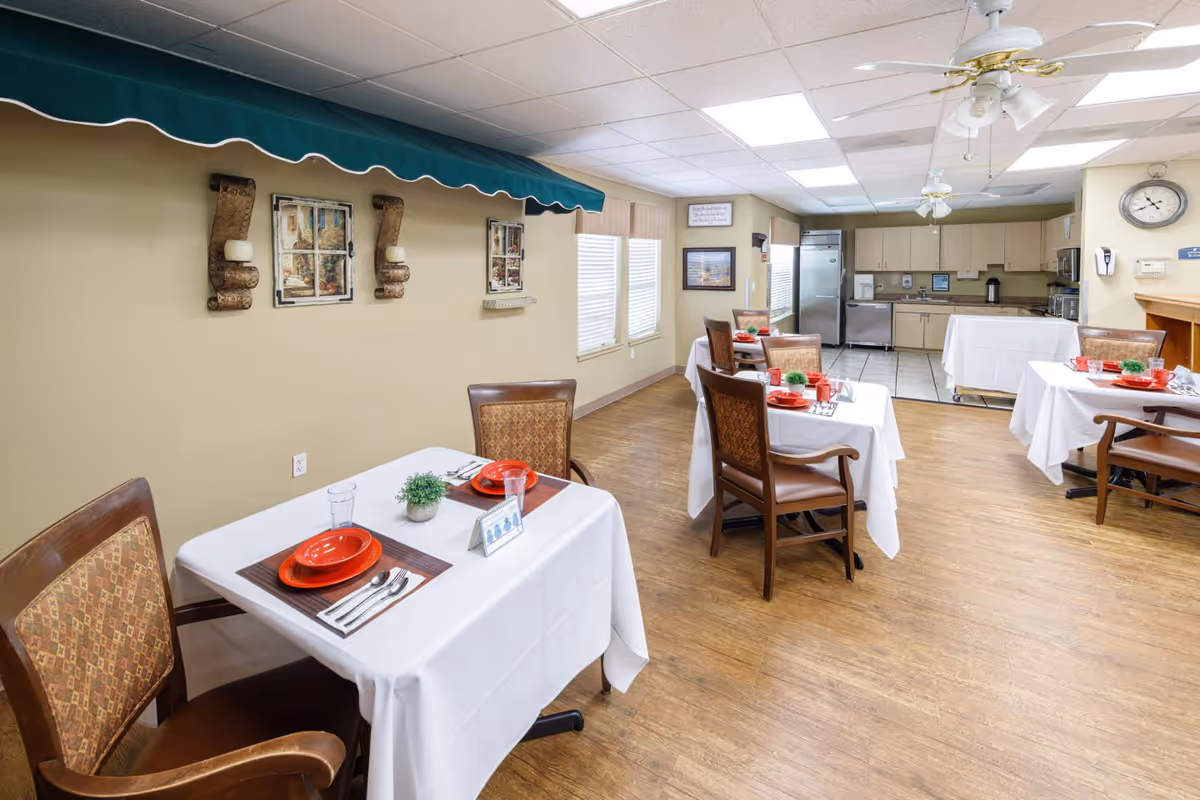 Communal dining room with small tables set with red dishes and a kitchenette in the background.