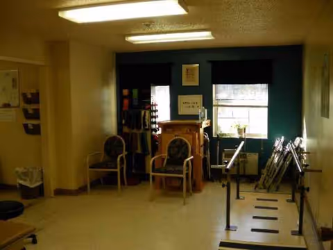 Dimly lit interior room in a nursing facility with chairs and exercise equipment.